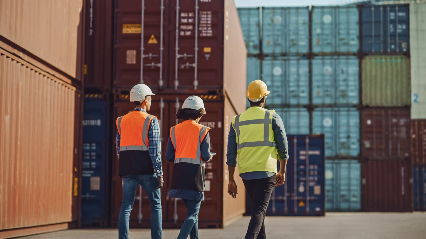 two men and woman walking in a shipping container yard image